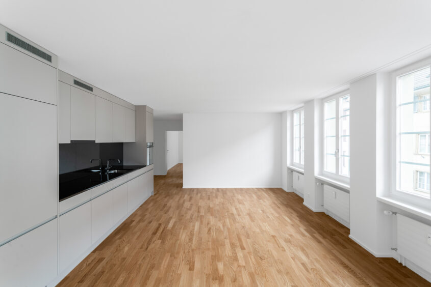 Moderne Architekturfotografie eines lichten Wohnbereichs mit weißer Küche, Holzboden und großen Fenstern